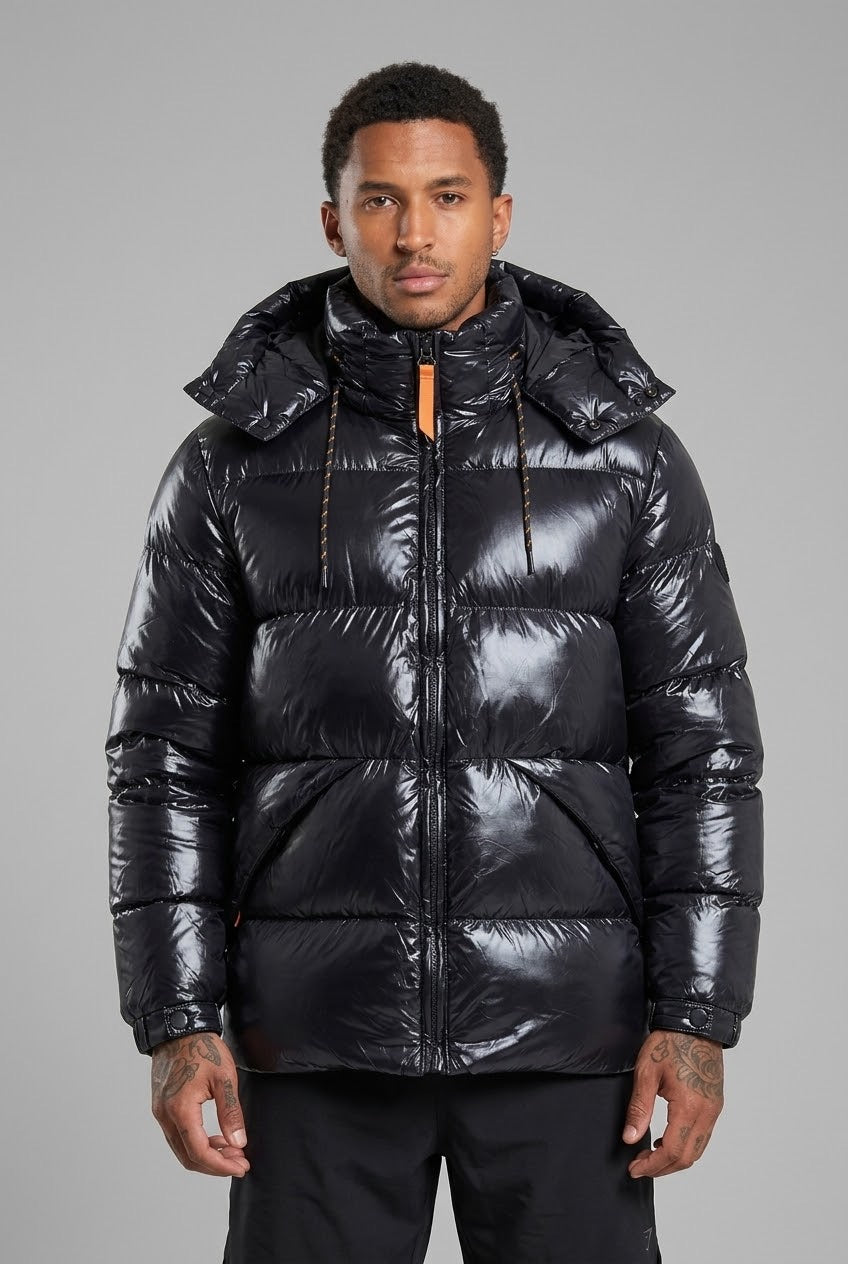 Homme portant une doudoune bonhomme noire brillante à capuche matelassée avec détails orange sur fond gris