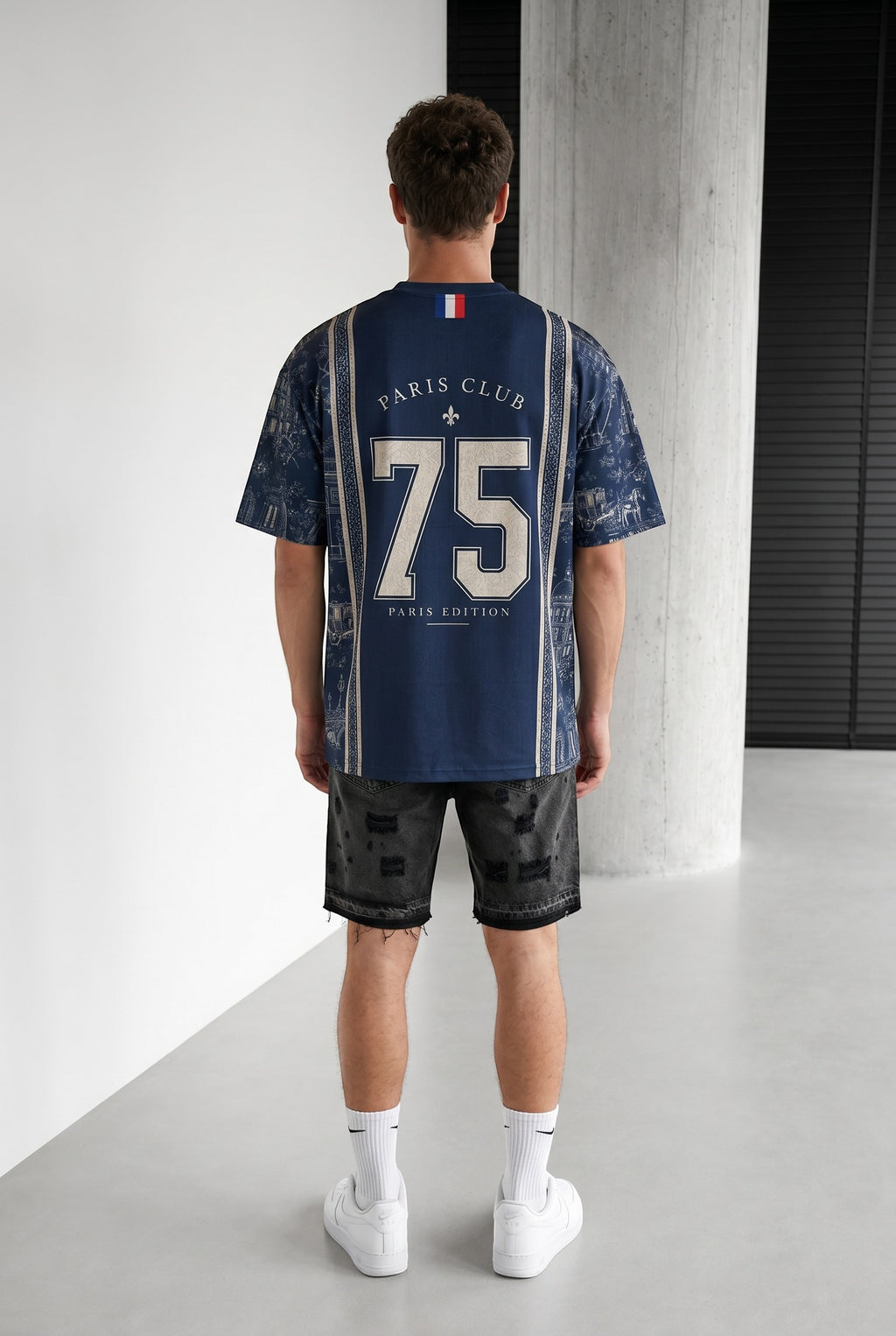 Homme portant un maillot bleu marine bonhomme avec le numéro 75 et des motifs parisiens au dos, coupe oversize.