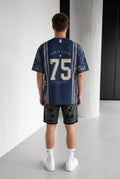 Homme portant un maillot bleu marine bonhomme avec le numéro 75 et des motifs parisiens au dos, coupe oversize.