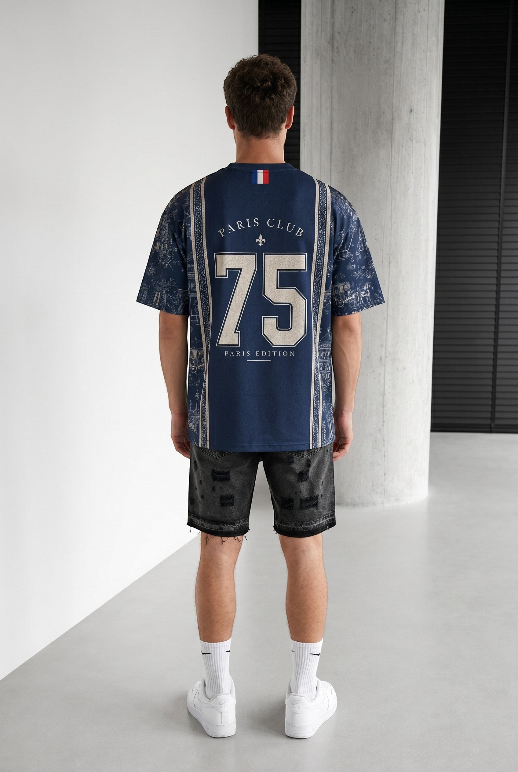 Homme portant un maillot bleu marine bonhomme avec le numéro 75 et des motifs parisiens au dos, coupe oversize.