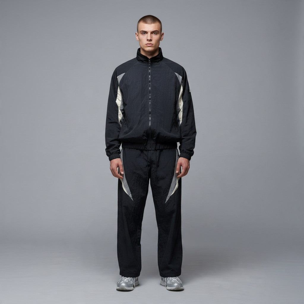 Homme portant un ensemble survêtement rétro bonhomme en nylon noir avec empiècements gris et écru, doublé polaire.